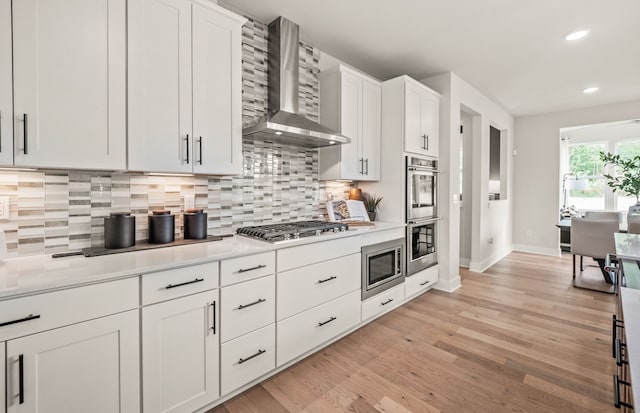 kitchen featuring wall chimney exhaust hood, stainless steel appliances, baseboards, tasteful backsplash, and light countertops