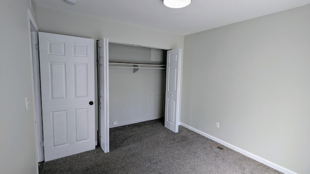 unfurnished bedroom featuring dark carpet, a closet, and baseboards