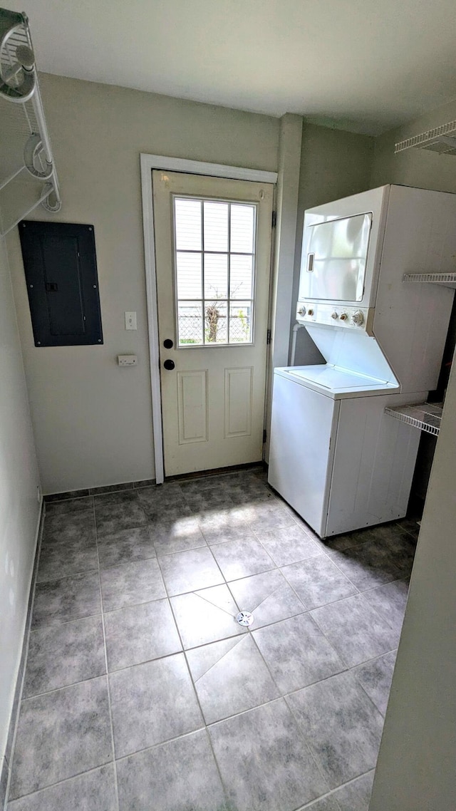 laundry room with stacked washer / drying machine, electric panel, light tile patterned flooring, and baseboards