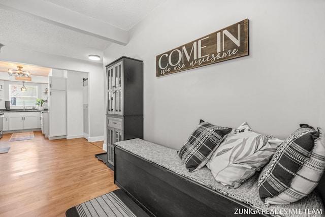 bedroom with light wood-style flooring, a chandelier, beamed ceiling, and a textured ceiling