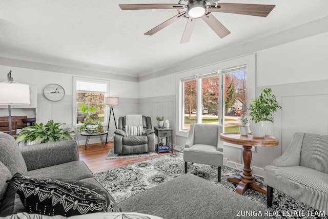 living area with wood finished floors, a ceiling fan, and wainscoting