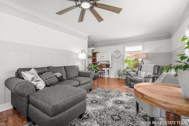 living room with a ceiling fan, a decorative wall, and wood finished floors