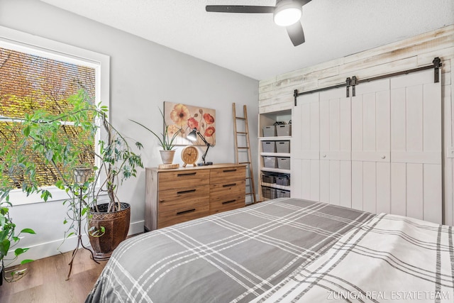 bedroom with a barn door, wood finished floors, and a ceiling fan