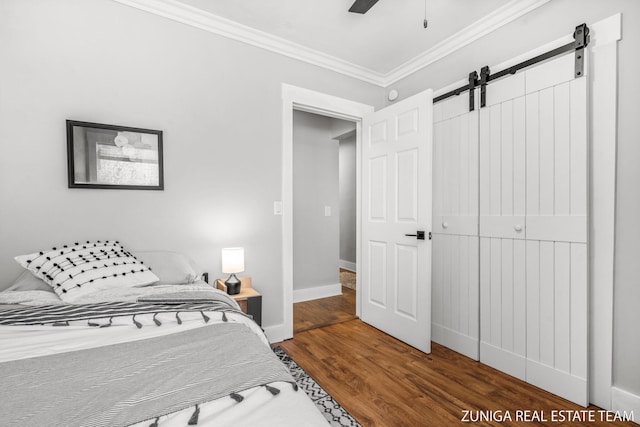 bedroom featuring crown molding, a barn door, wood finished floors, baseboards, and ceiling fan