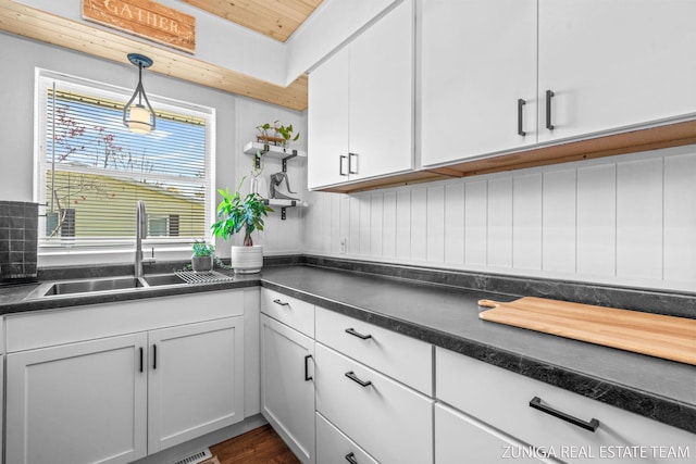 kitchen featuring a sink, white cabinets, dark countertops, hanging light fixtures, and open shelves