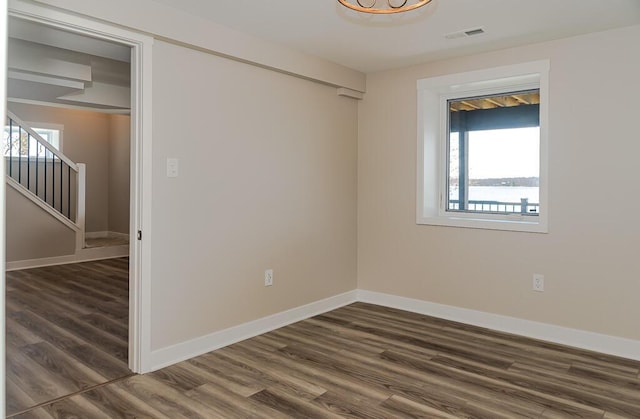 empty room with dark wood-style floors, plenty of natural light, baseboards, and stairs