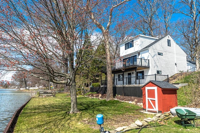 view of grassy yard featuring a storage shed, an outbuilding, a water view, and a balcony