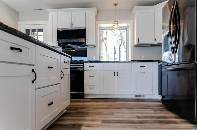 kitchen with black refrigerator with ice dispenser, white cabinetry, a sink, and decorative light fixtures