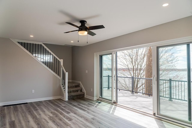 unfurnished living room with wood finished floors, stairway, ceiling fan, baseboards, and recessed lighting