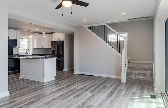 kitchen featuring black fridge with ice dispenser, stove, light wood-style flooring, white cabinets, and recessed lighting