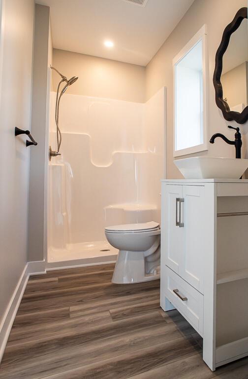 full bath featuring a shower, wood finished floors, toilet, and vanity
