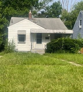 rear view of house with a chimney, a lawn, and covered porch