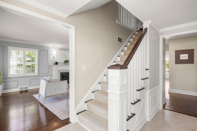 stairs with ornamental molding, a glass covered fireplace, wood finished floors, and baseboards