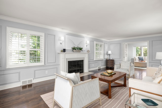living area with a decorative wall, ornamental molding, wood finished floors, and a fireplace with flush hearth