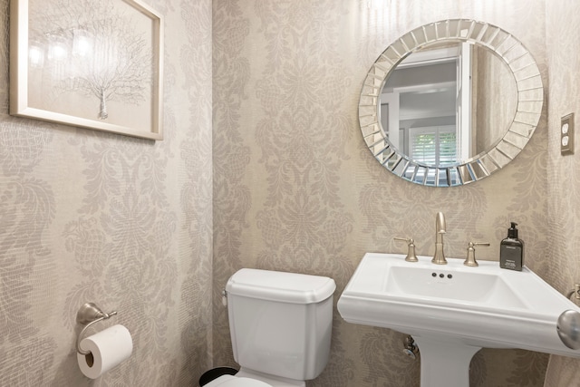 half bath with wallpapered walls, toilet, and a sink