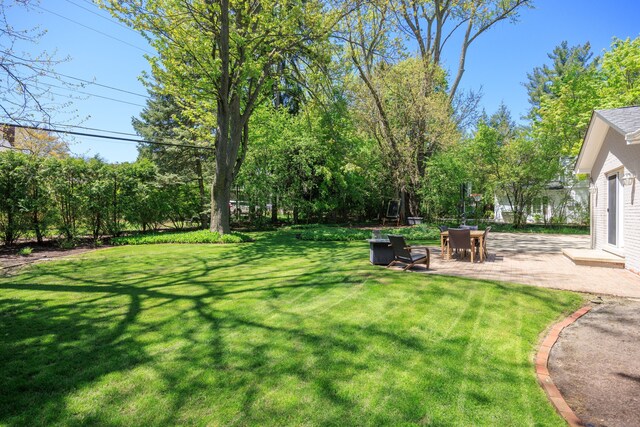 view of green lawn with a patio and view of wooded area