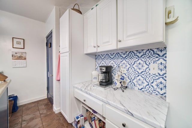 1621 W Beyer Rd, Ludington, MI 49431 - kitchen with white cabinetry, baseboards, decorative backsplash, light stone countertops, and stone finish flooring