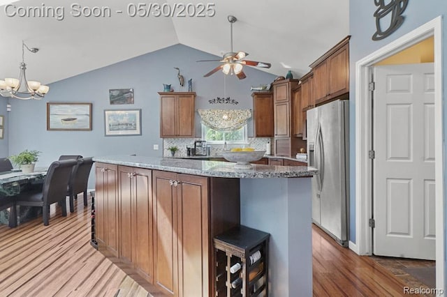 9450 Sandlewood Ct, Whitmore Lake, MI 48189 - kitchen featuring stainless steel fridge, vaulted ceiling, a ceiling fan, wood finished floors, and a chandelier