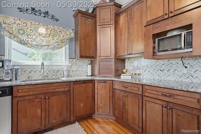 9450 Sandlewood Ct, Whitmore Lake, MI 48189 - kitchen with stainless steel appliances, a sink, brown cabinets, light wood-style flooring, and light stone countertops