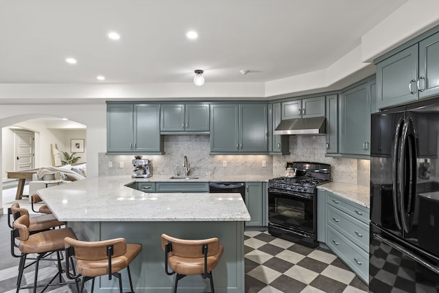 kitchen featuring black appliances, arched walkways, light floors, a kitchen breakfast bar, and recessed lighting