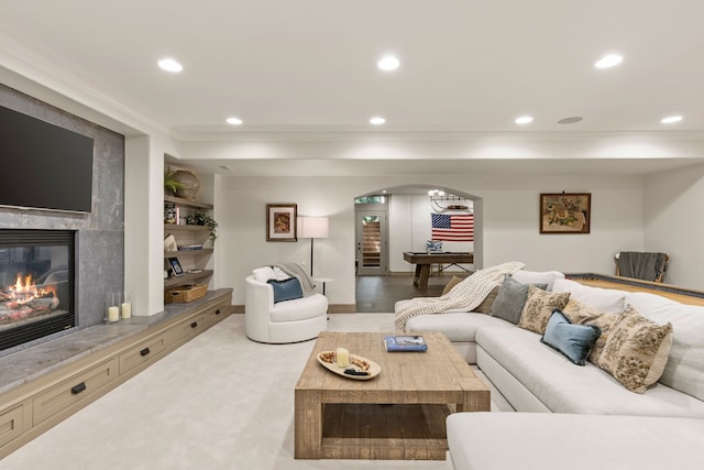 carpeted living room featuring crown molding, arched walkways, recessed lighting, and a premium fireplace