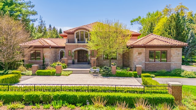 mediterranean / spanish home with a tile roof, a fenced front yard, and stone siding