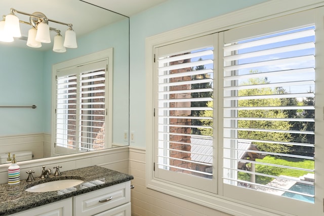 half bath with healthy amount of natural light, vanity, and a wainscoted wall