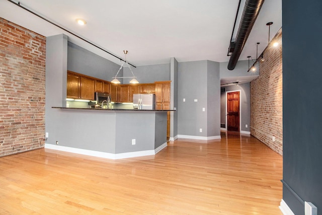 kitchen with stainless steel appliances, brick wall, light wood finished floors, dark countertops, and decorative light fixtures