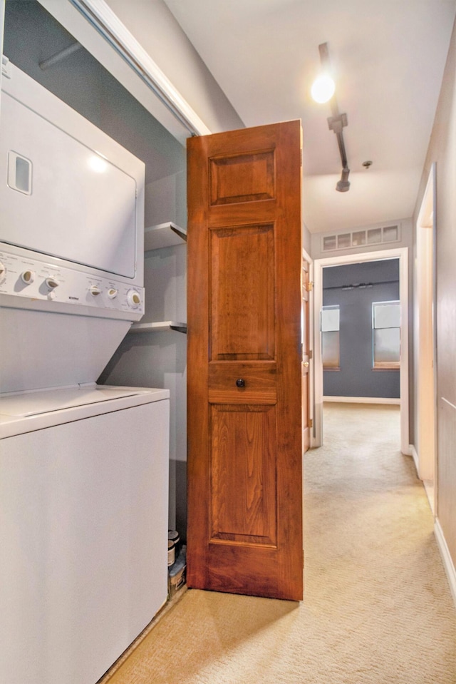 laundry room featuring stacked washer / drying machine, light colored carpet, and baseboards