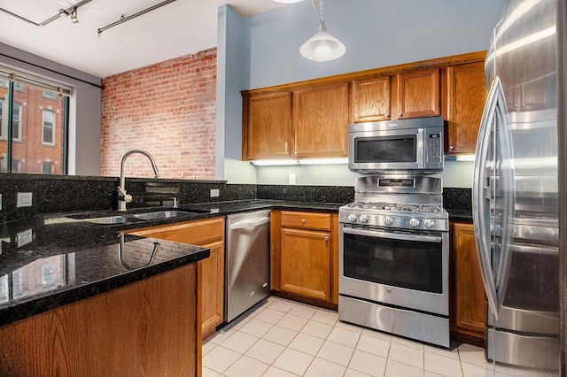kitchen with stainless steel appliances, a sink, light tile patterned floors, brown cabinets, and hanging light fixtures
