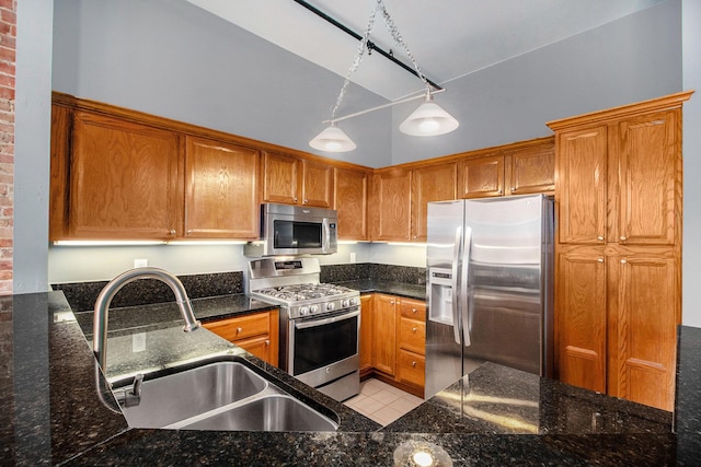 kitchen with appliances with stainless steel finishes, a sink, brown cabinetry, and dark stone countertops
