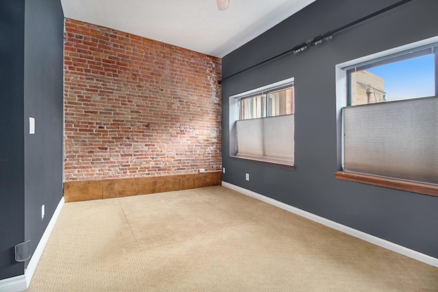 carpeted empty room featuring brick wall and baseboards