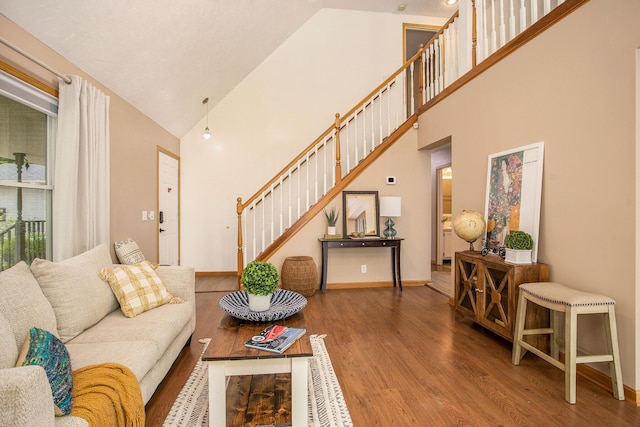 living area with wood finished floors, high vaulted ceiling, stairway, and baseboards