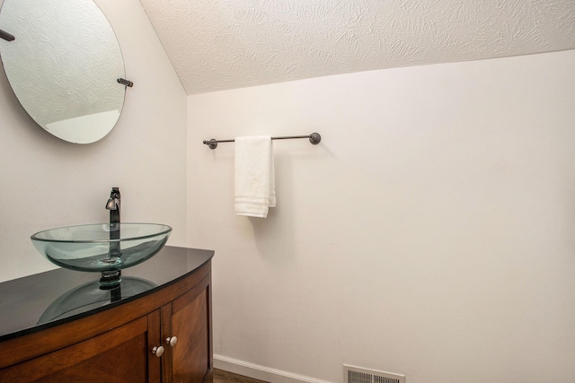 bathroom featuring a sink, a textured ceiling, baseboards, and vaulted ceiling