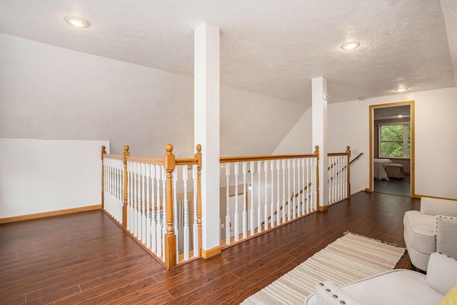 hallway with an upstairs landing, wood finished floors, a textured ceiling, and baseboards