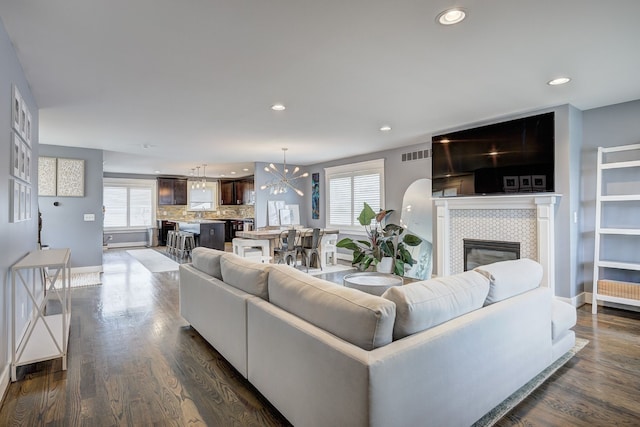 living area featuring a chandelier, a tiled fireplace, healthy amount of natural light, dark wood-style flooring, and recessed lighting