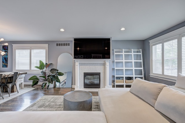 living room featuring healthy amount of natural light, wood finished floors, a tiled fireplace, baseboards, and recessed lighting