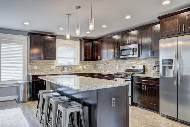 kitchen featuring stainless steel appliances, a breakfast bar, a center island, dark brown cabinets, and light stone countertops