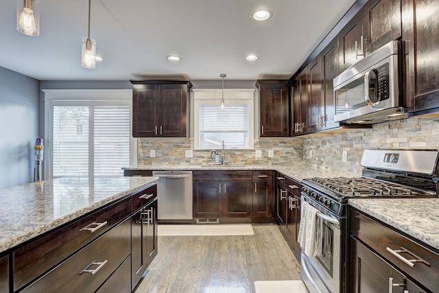 kitchen with appliances with stainless steel finishes, a sink, light wood finished floors, dark brown cabinets, and recessed lighting
