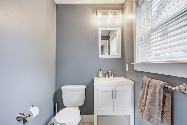 half bathroom featuring toilet, baseboards, and vanity