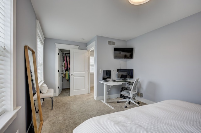 carpeted bedroom featuring baseboards, a walk in closet, a desk, and a closet