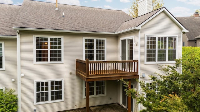 back of house with roof with shingles, a chimney, and a deck