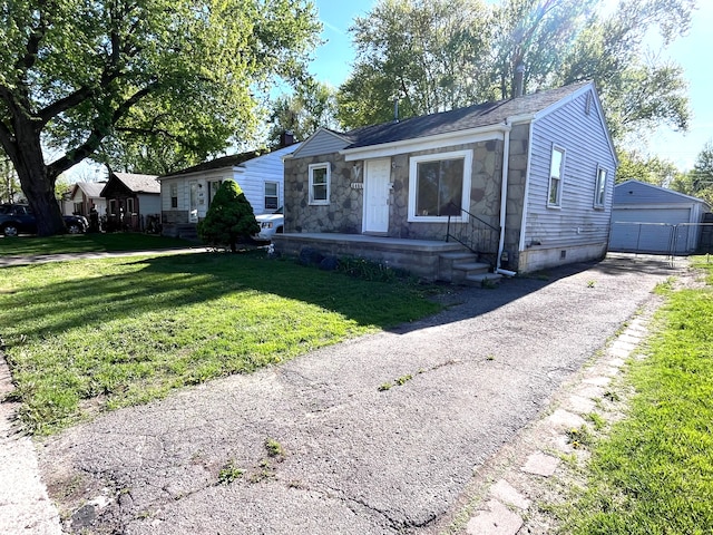 view of front of property featuring a front lawn, an outbuilding, a detached garage, stone siding, and roof with shingles