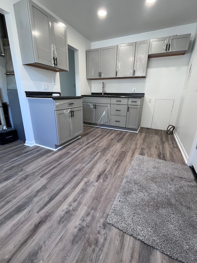 kitchen featuring gray cabinetry, dark countertops, a sink, dark wood-type flooring, and baseboards