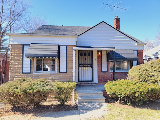 bungalow-style house with a chimney, brick siding, and a shingled roof