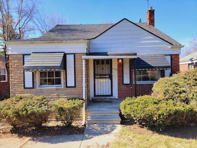 bungalow-style house featuring brick siding, a chimney, and roof with shingles