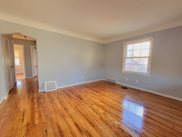 empty room with light wood-type flooring, baseboards, and arched walkways