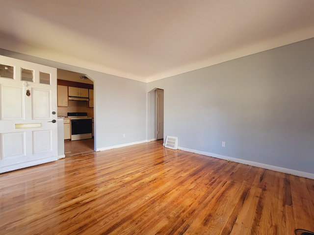empty room with light wood-style flooring, baseboards, and arched walkways
