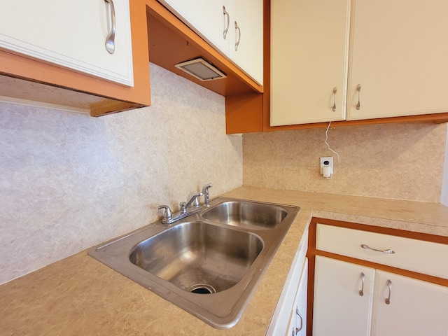 kitchen featuring a sink, light countertops, decorative backsplash, and white cabinetry