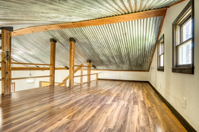additional living space with wood finished floors, vaulted ceiling, baseboards, and a textured wall